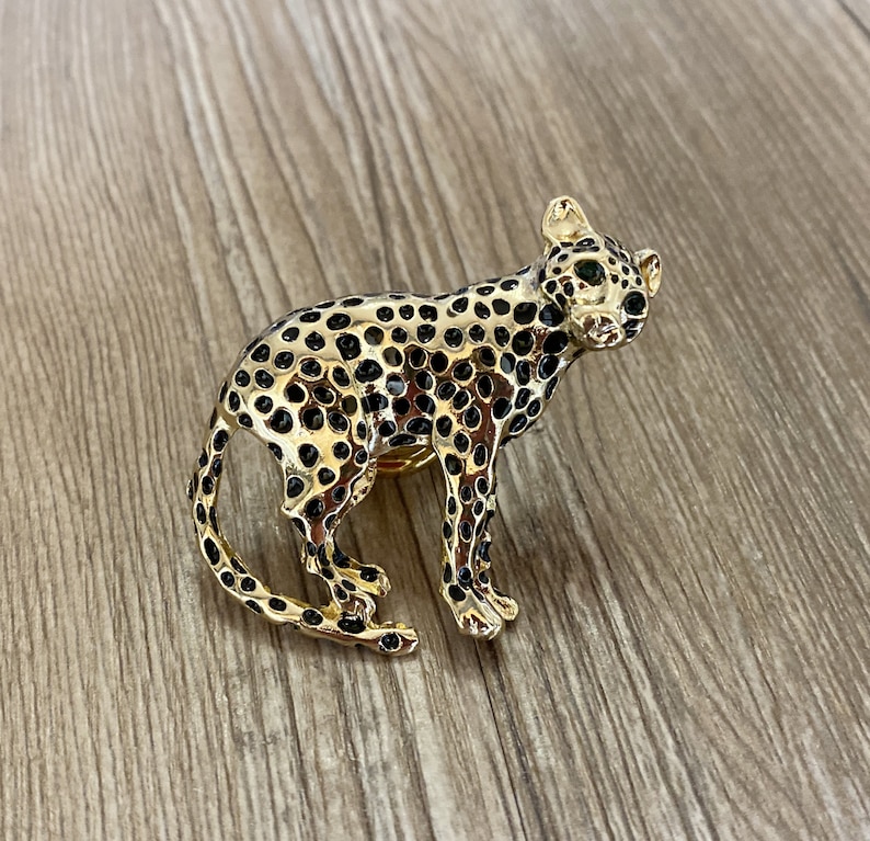 Peut inclure: Une figurine de l&eacute;opard dor&eacute;e avec des taches noires et des yeux verts. La figurine est pos&eacute;e sur une surface en bois.