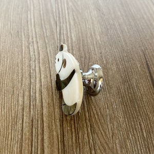 Puede incluir: Un pomo de armario de panda blanco y negro con base plateada.