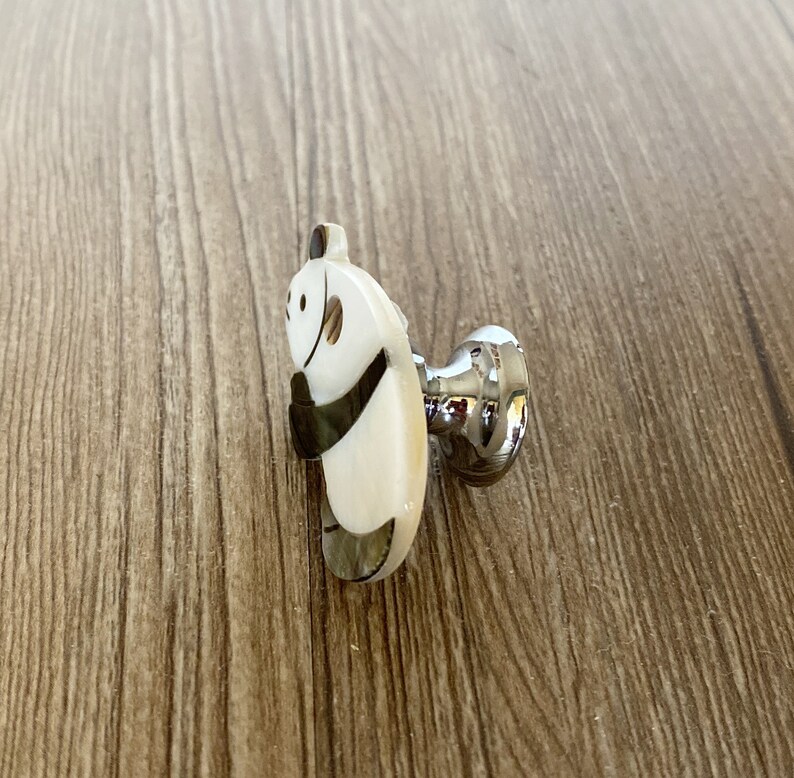 Puede incluir: Un pomo de armario de panda blanco y negro con base plateada.