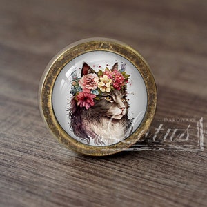 Peut inclure: Un bouton de porte rond en laiton avec un insert en verre représentant une illustration aquarelle d'un chat portant une couronne de fleurs. Le chat a un pelage brun et blanc et des yeux verts.