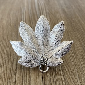 May include: Silver-toned metal leaf charm with a detailed textured surface and a small loop at the bottom.