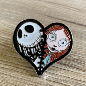 May include: A black and white heart-shaped pin with a cartoon image of Jack Skellington and Sally from the Nightmare Before Christmas movie. The pin is broken in half, with Jack on the left side and Sally on the right side.