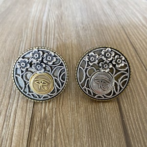 以下が含まれることがあります： ホルスの目のデザインと花のアクセントが付いた、銀と金の2つの金属製のリングです。