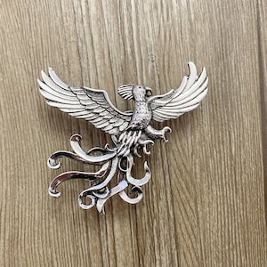 Op de afbeelding: Een zilveren phoenix broche met ingewikkelde details. De phoenix is afgebeeld met zijn vleugels gespreid en zijn staartveren die erachter stromen.