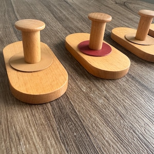 May include: Three wooden wall hooks with a red and brown circular base. The hooks are made of natural wood and have a simple design.