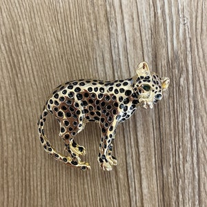 Peut inclure: Une broche dor&eacute;e en forme de l&eacute;opard avec des taches noires et des yeux verts.