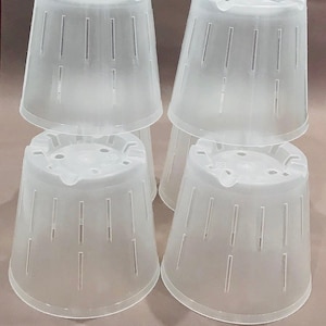 Pode incluir: Quatro vasos de plantas de plástico transparente empilhados. Cada vaso tem uma forma cónica com fendas verticais para drenagem. Os vasos têm um topo canelado e uma base ligeiramente alargada. Os vasos são translúcidos.