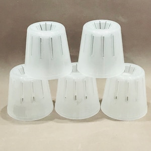 May include: Five white plastic plant pots with drainage holes. The pots are stacked in a pyramid shape.