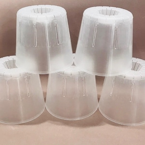 Puede incluir: Una pila de cinco objetos de plástico blanco translúcido en forma de cono. Cada cono tiene una parte superior ancha y circular con ranuras verticales y un cuerpo cónico con ranuras verticales. Los objetos están dispuestos en forma de pirámide.