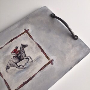 May include: A gray wooden serving tray with a black metal handle. The tray features a painted image of a jockey riding a horse, framed by a decorative border.