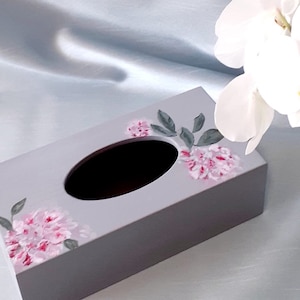 Könnte beinhalten: Ein grauer Taschentuchbox-Bezug mit einem Blumendesign. Das Design zeigt rosa Blumen und grüne Blätter.