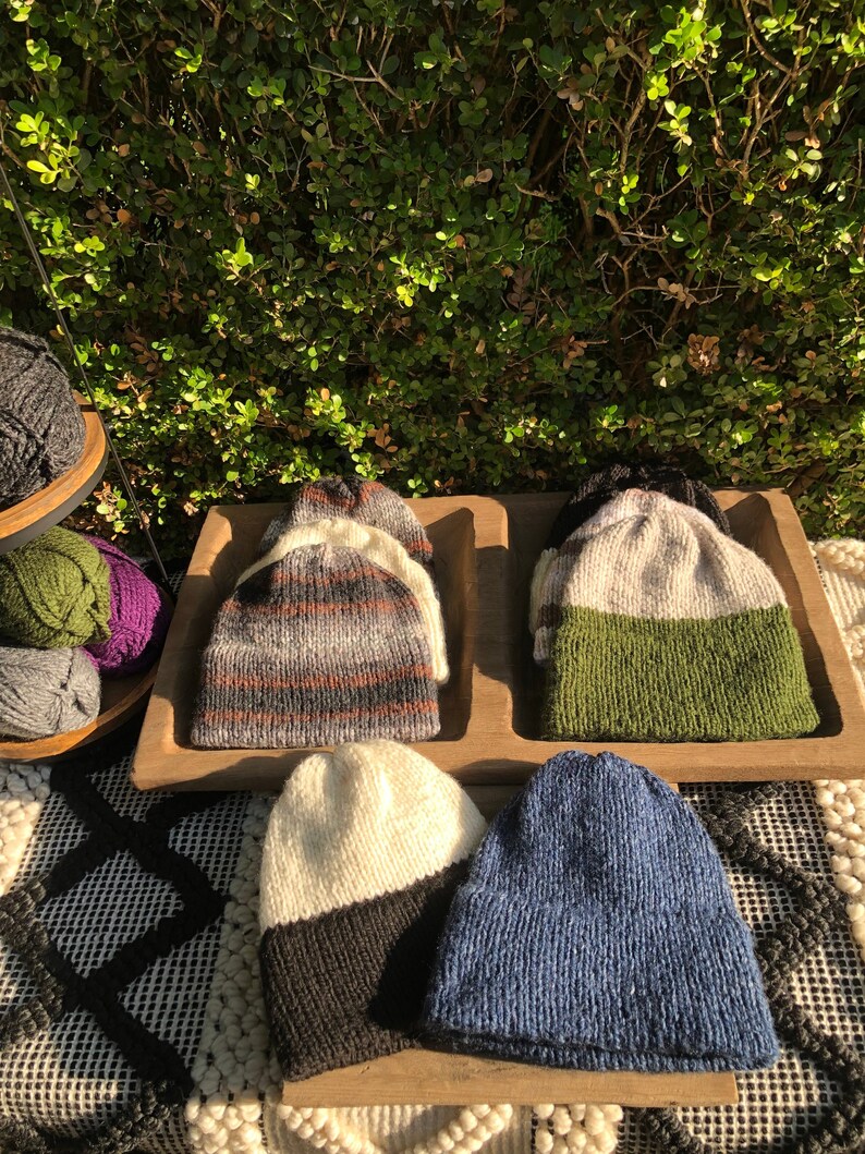 May include: Four knitted hats in different colors and patterns. The hats are displayed on a wooden tray. The hats are made of wool and have a variety of textures.