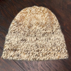 May include: A beige and brown knit beanie hat with a textured knit pattern.