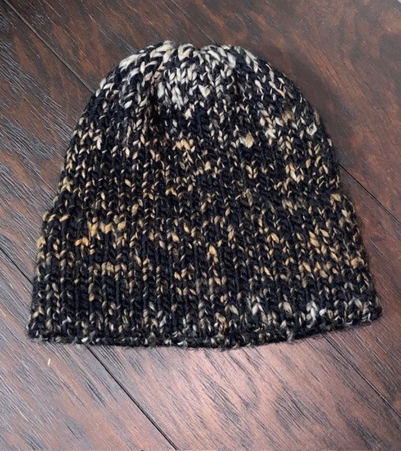 May include: A black, white, and brown knit beanie hat. The hat is made of a soft, textured yarn.