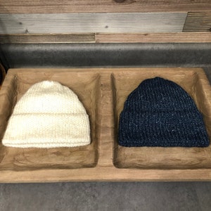 May include: Two knitted hats in a wooden tray. One hat is white and the other is dark blue.