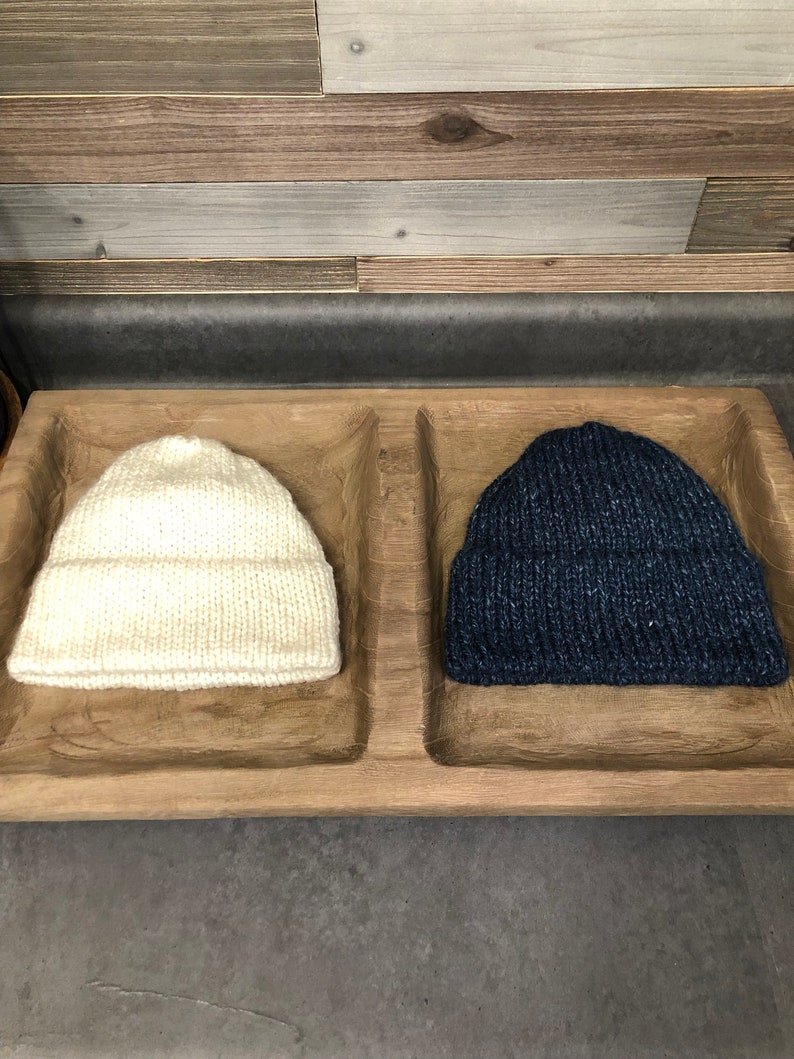 May include: Two knitted hats in a wooden tray. One hat is white and the other is dark blue.