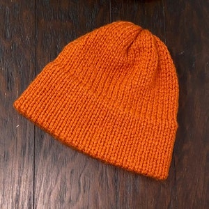 May include: A bright orange knitted beanie hat. The hat is made of a soft, warm material and has a simple, classic design.