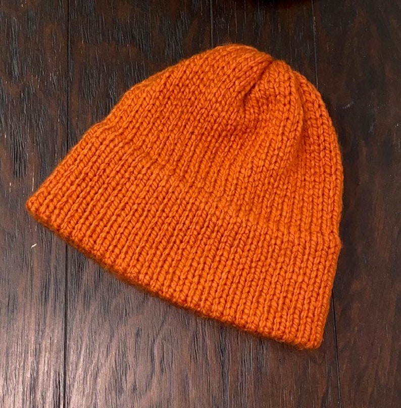 May include: A bright orange knitted beanie hat. The hat is made of a soft, warm material and has a simple, classic design.
