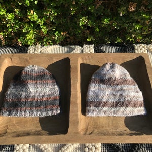 May include: Two knitted hats in a wooden tray. One hat is black, white, and brown striped. The other hat is brown, white, and gray striped.