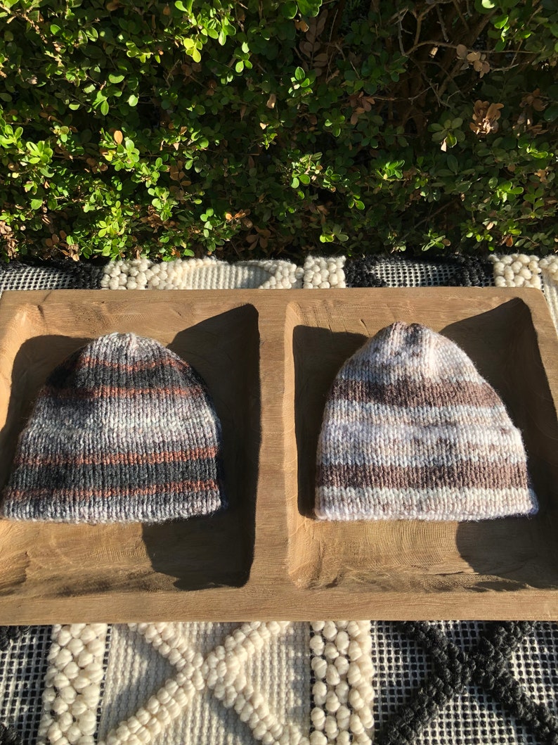 May include: Two knitted hats in a wooden tray. One hat is black, white, and brown striped. The other hat is brown, white, and gray striped.