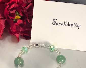 May include: A green and clear beaded bracelet with a silver bead. The bracelet has a card behind it with the text "Sarahadipity" written in cursive.