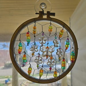 May include: A handmade dreamcatcher with a gold-colored embroidery hoop. The dreamcatcher features a black web design with clear flower and butterfly-shaped beads. Colorful beaded strands hang from the bottom, adding a vibrant touch to the decor.