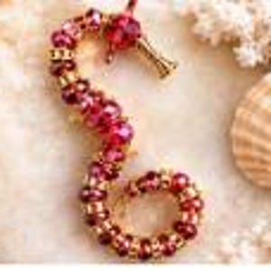 May include: A seahorse-shaped brooch crafted from deep red faceted beads and small gold-toned metal spacers. The design features a curved body with a prominent red bead for the eye and a gold-toned snout, creating a detailed aquatic creature.