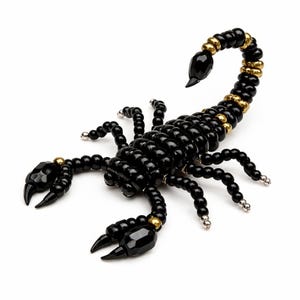 May include: A black beaded scorpion sculpture with gold and silver detailing. The scorpion's body is formed from small, round beads, with larger, faceted beads creating the claws and stinger. The sculpture is set against a white backdrop.
