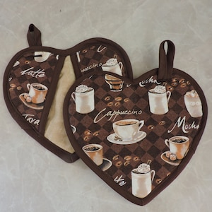 May include: Two brown heart-shaped pot holders with a coffee theme. The pot holders feature a checkered pattern with coffee beans and various coffee drinks, including latte, cappuccino, and mocha.