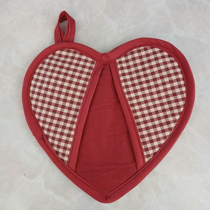 May include: Heart-shaped red and white checkered pot holder with a loop for hanging. The pot holder has a solid red center and a red border. Kitchen and dining accessory.