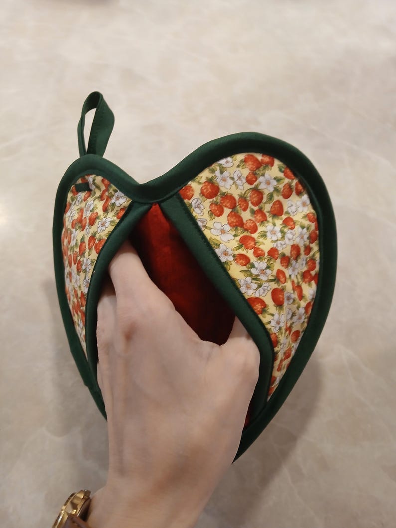 Pu&ograve; includere: Un guanto da forno a forma di cuore verde e rosso con un motivo a fragole e fiori. Il guanto da forno ha un anello per appenderlo.