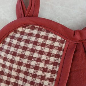 May include: Close-up of a burgundy and cream checkered potholder with a burgundy trim and hanging loop. The potholder has a classic gingham pattern and is made of fabric.