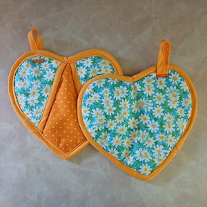 May include: Two heart-shaped pot holders. One is orange with white polka dots and a blue and white floral pattern. The other is blue with a white daisy pattern.