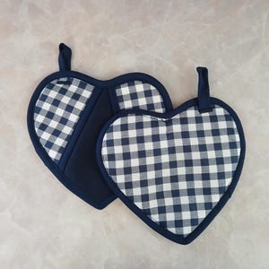 May include: Two heart-shaped pot holders. The pot holders have a navy blue and white gingham pattern. The edges and hanging loops are navy blue. The pot holders are made of fabric.