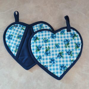 Puede incluir: Dos agarraderas en forma de corazón. Las agarraderas tienen un patrón de cuadros azules y blancos con ilustraciones de arándanos azules. Los bordes y las trabillas para colgar son de color azul marino. Diseñado para uso en la cocina.
