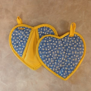 May include: Two yellow and blue heart-shaped pot holders with a white daisy pattern.