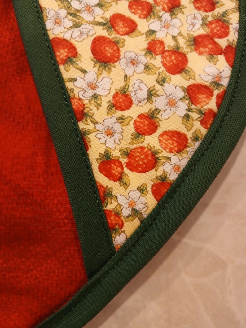 Pu&ograve; includere: Primo piano di un bordo di tessuto verde con uno sfondo di tessuto giallo che presenta un motivo ripetuto di fragole rosse e fiori bianchi.