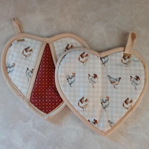 May include: Two heart-shaped pot holders with a chicken print. One pot holder is red with white polka dots and the other is white with a light blue and white gingham pattern.