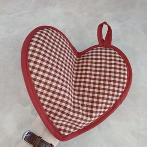 May include: Heart-shaped pot holder with a red and white checkered pattern. The pot holder has a red border and a loop for hanging. Kitchen and dining accessory.