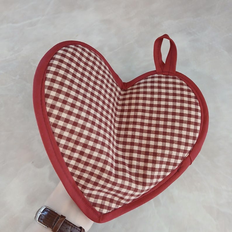 May include: Heart-shaped pot holder with a red and white checkered pattern. The pot holder has a red border and a loop for hanging. Kitchen and dining accessory.