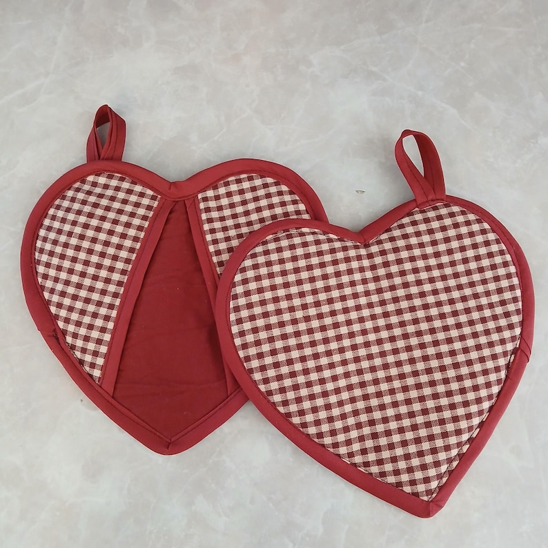 May include: Two heart-shaped potholders. The potholders have a red gingham pattern with a solid red border and a loop for hanging. The potholders are red and white.