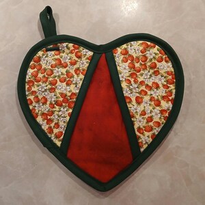Pu&ograve; includere: Un guanto da forno a forma di cuore rosso e verde con una stampa di fragole. Il guanto da forno ha un anello per appenderlo.