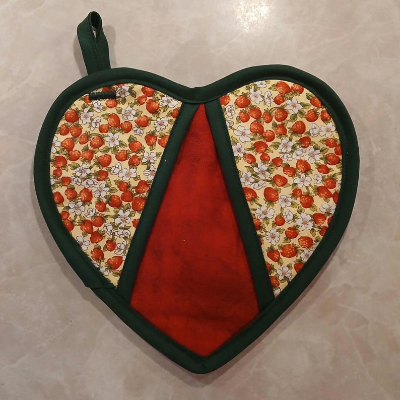 Pu&ograve; includere: Un guanto da forno a forma di cuore rosso e verde con una stampa di fragole. Il guanto da forno ha un anello per appenderlo.