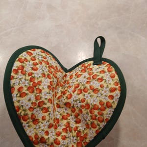 Pu&ograve; includere: Un sottopentola a forma di cuore con un bordo verde e uno sfondo giallo con un motivo di fragole e fiori.