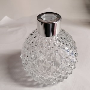 May include: A clear glass diffuser bottle with a silver lid. The bottle has a textured, diamond-shaped pattern.