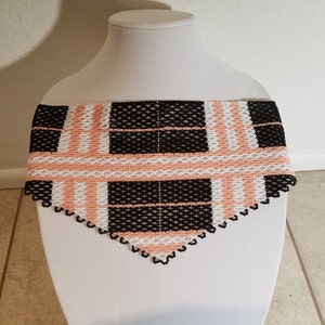 May include: A black, white, and peach beaded necklace with a plaid pattern. The necklace is triangular in shape and has a scalloped edge.