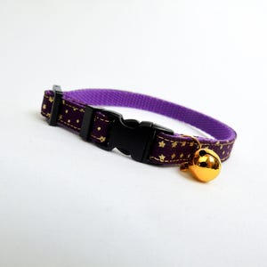 Puede incluir: Collar de gato morado con estrellas doradas y una campanita dorada. El collar tiene una hebilla negra ajustable.