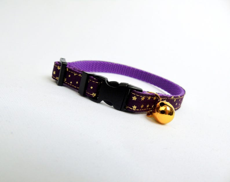 Puede incluir: Collar de gato morado con estrellas doradas y una campanita dorada. El collar tiene una hebilla negra ajustable.