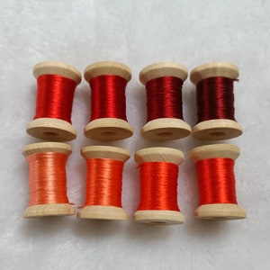Puede incluir: Ocho carretes de hilo en varios tonos de rojo y naranja, enrollados en carretes de madera.