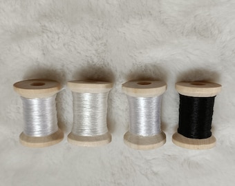 May include: Four spools of thread on wooden bobbins. Three spools are white and one is black.